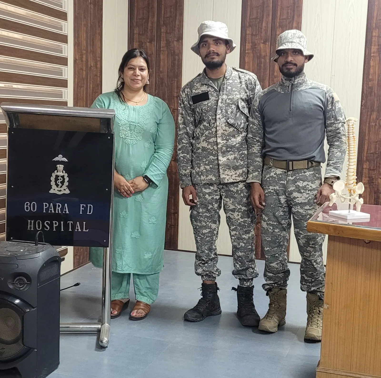 AvaTrita clinician standing with two soldiers beside a 60 Para Field Hospital lectern, a spine model on the table alongside